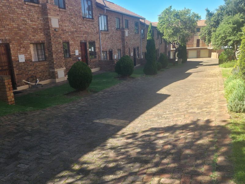 Exterior view of a face brick apartment complex featuring a paved driveway, landscaped garden beds, and secure unit entrances.