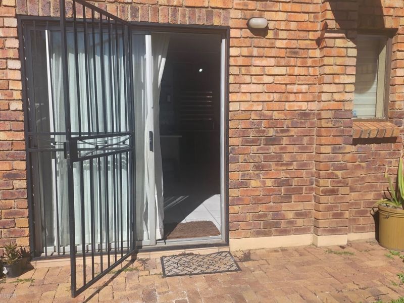 Rear exterior view of an apartment featuring a face brick facade, paved patio area, and a secure sliding glass door entrance.