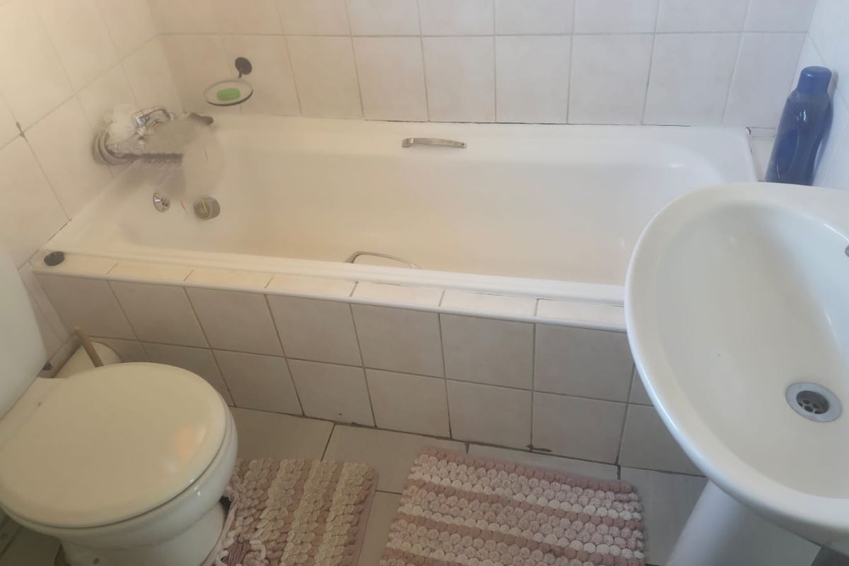 A functional bathroom featuring a standard bathtub, pedestal basin, and toilet with tiled walls and flooring.