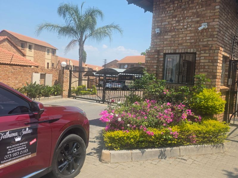 The entrance to the apartment complex features a brick guardhouse, secure gated access, and paved driveway with established landscaping.