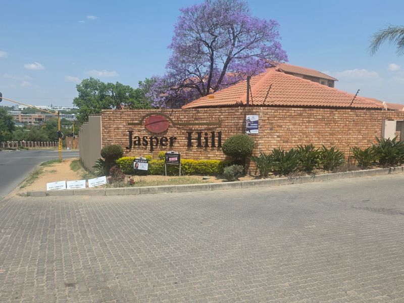 Street view of the Jasper Hill complex entrance featuring a brick boundary wall, electric fencing, and paved access area.