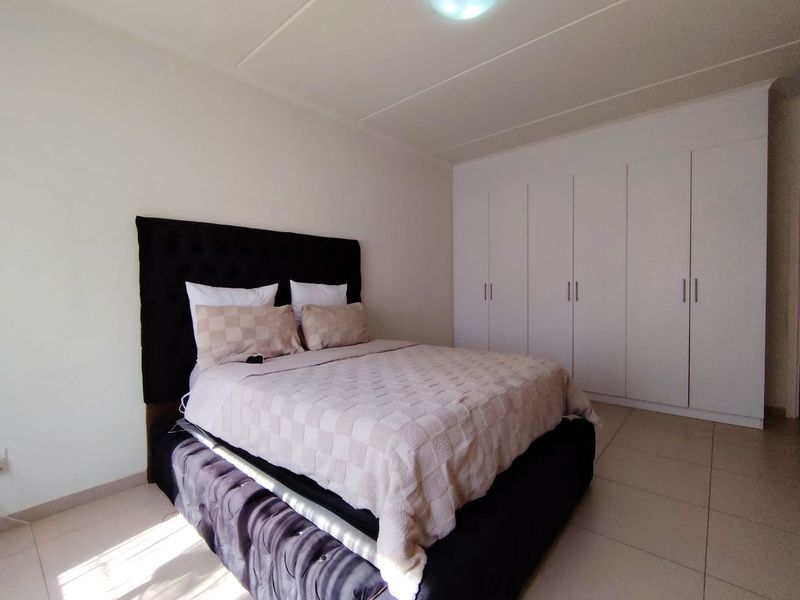 A well-maintained bedroom featuring neutral tiled flooring and extensive white built-in cupboards providing ample storage space.