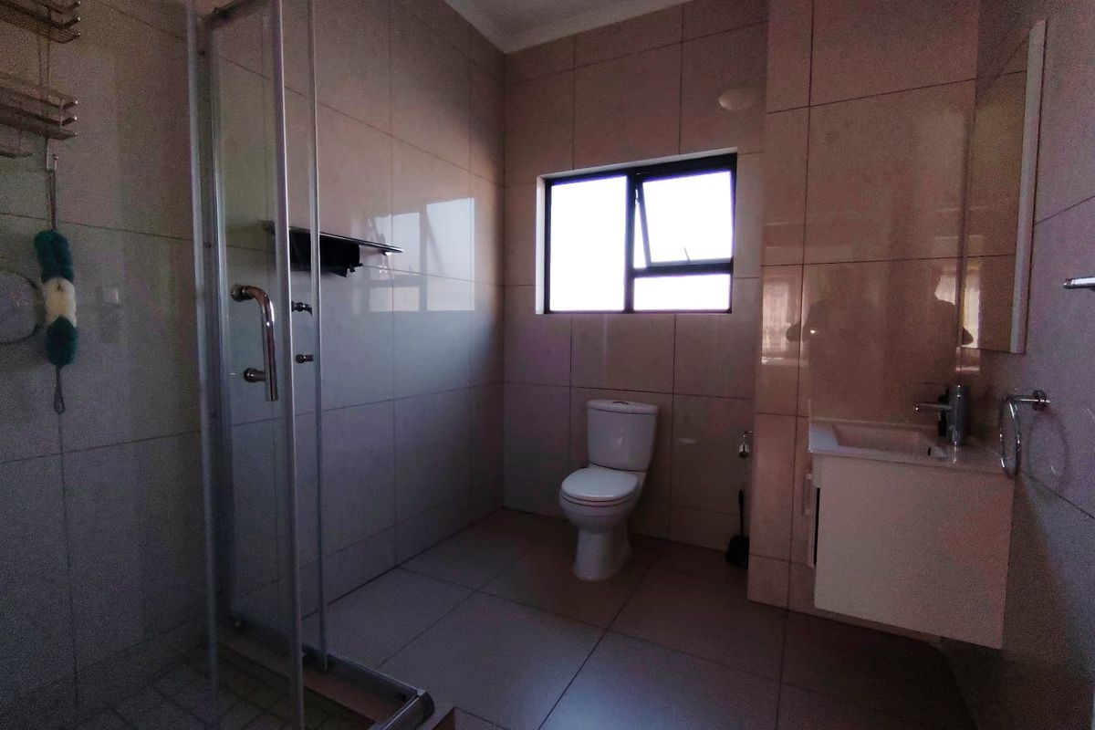 A clean, modern bathroom featuring a glass-enclosed shower, a wall-mounted vanity with basin, and neutral floor-to-ceiling tiling.