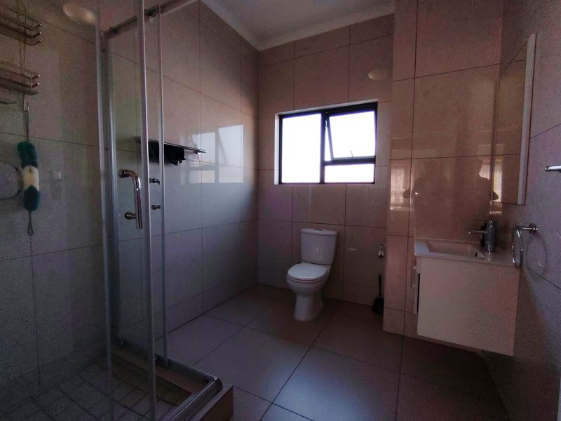 A clean, modern bathroom featuring a glass-enclosed shower, a wall-mounted vanity with basin, and neutral floor-to-ceiling tiling.