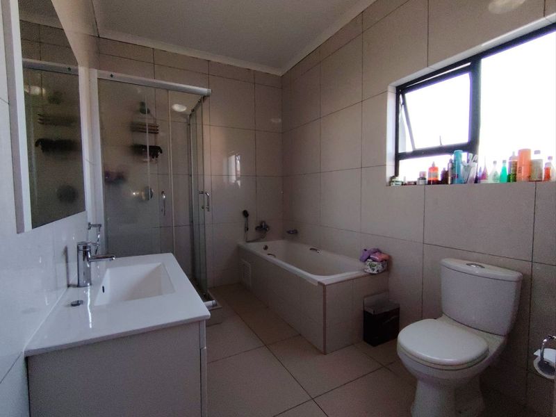 A modern bathroom featuring a tiled finish, a vanity with basin, a glass shower enclosure, a bathtub, and a toilet.