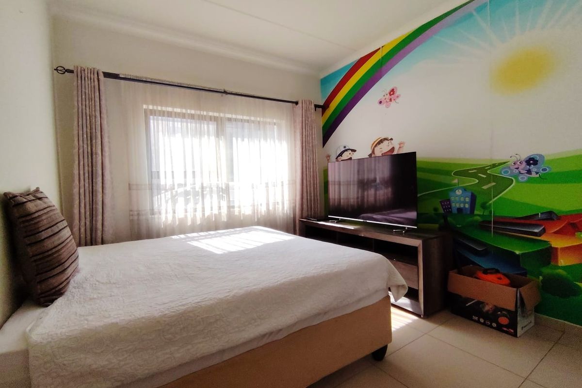 A bedroom featuring tiled flooring and a large window with curtain rails, currently decorated with a vibrant wall mural.