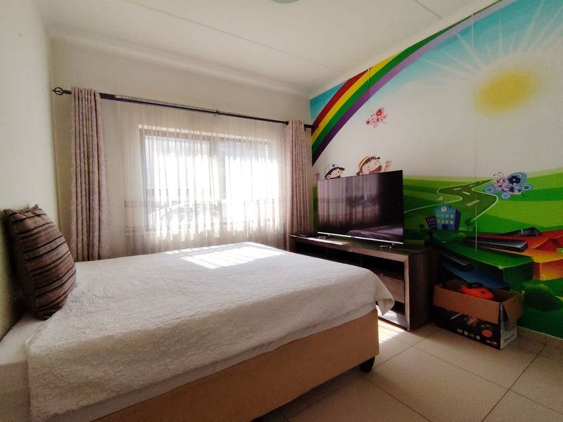 A bedroom featuring tiled flooring and a large window with curtain rails, currently decorated with a vibrant wall mural.