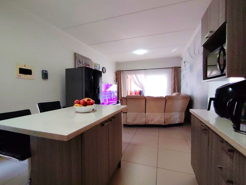 Open-plan living area featuring a kitchen with island, tiled flooring, and integrated cabinetry, flowing into a comfortable lounge space with natural light.
