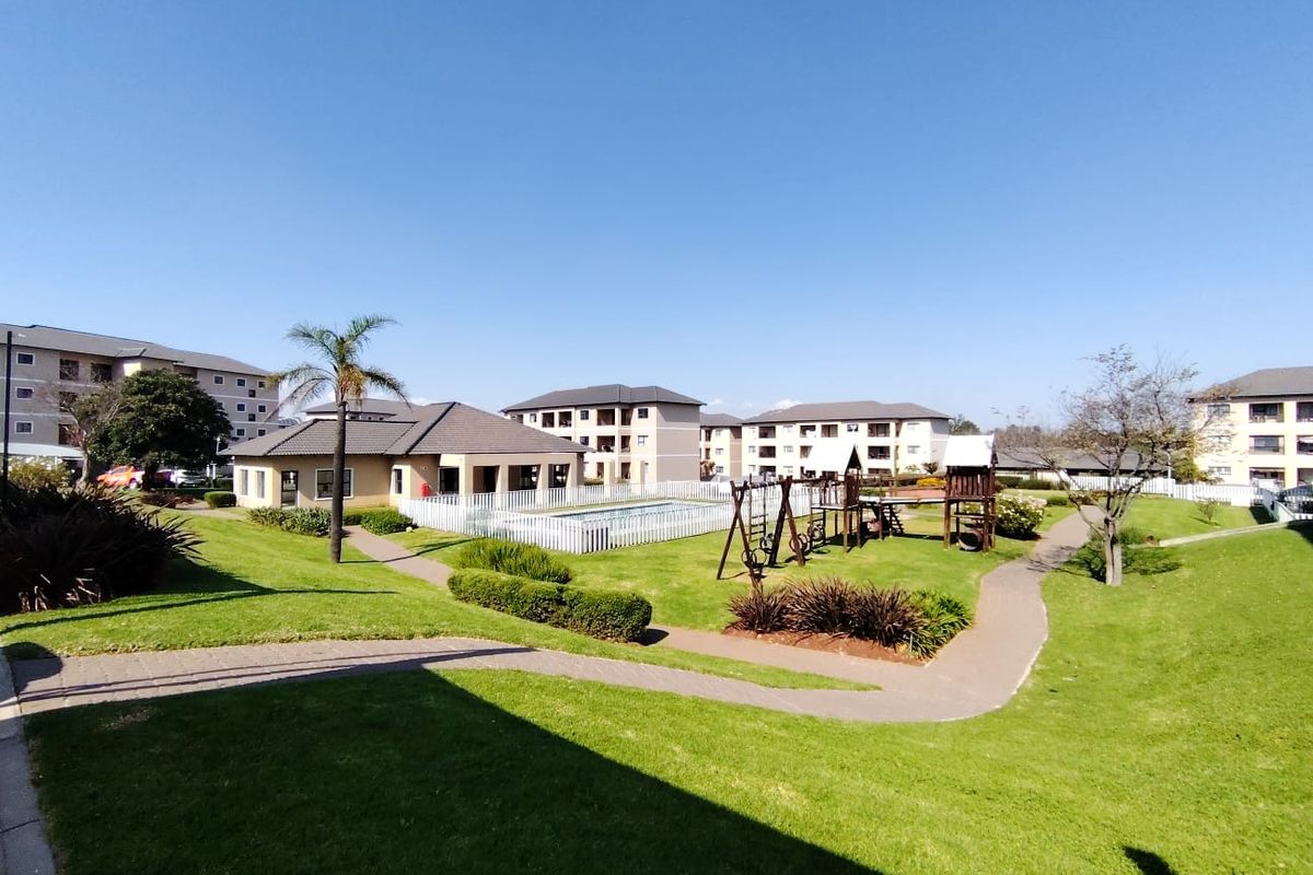 A well-maintained communal garden area featuring paved walkways, a swimming pool, and playground facilities within an apartment complex.