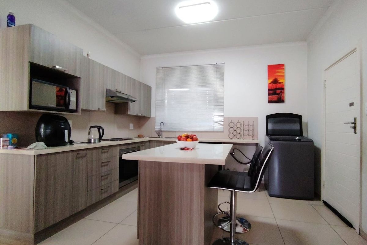 Modern kitchen featuring wood-finish cabinetry, a central island, built-in oven, extractor fan, and tiled flooring with ample counter space.