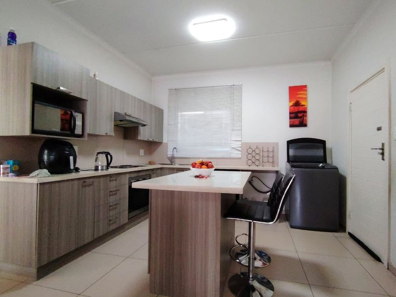 Modern kitchen featuring wood-finish cabinetry, a central island, built-in oven, extractor fan, and tiled flooring with ample counter space.