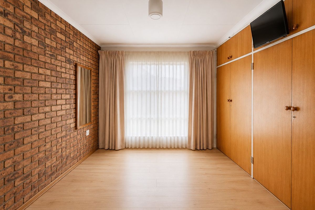 A well-maintained bedroom featuring a distinctive exposed brick feature wall, light wood-look flooring, and extensive built-in wooden cabinetry.