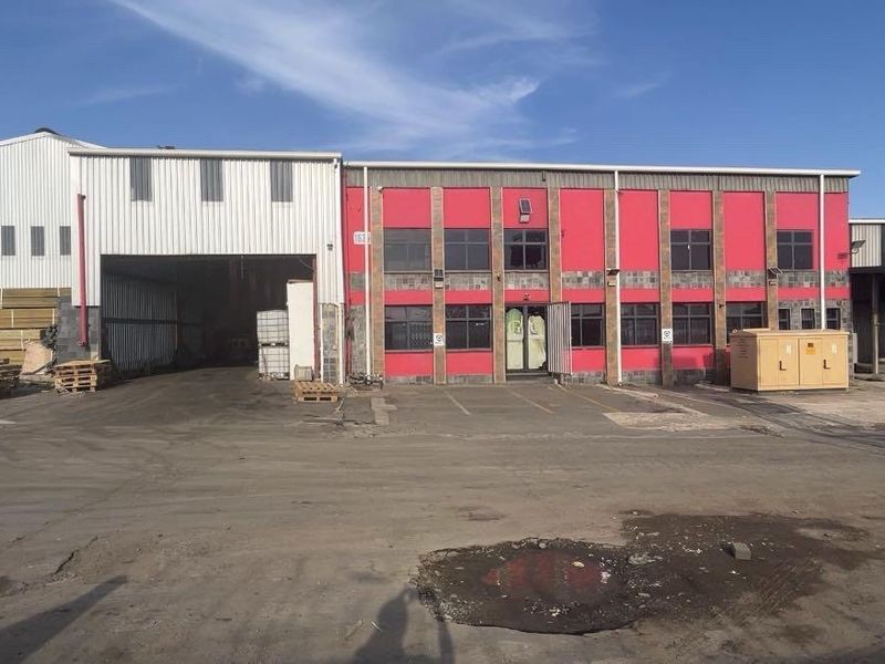 Industrial property featuring a large warehouse with metal cladding, a brick office facade, and an expansive asphalt yard area.