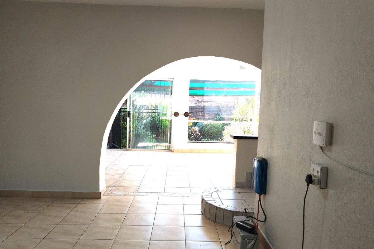 An empty living area featuring tiled flooring, an arched architectural opening, and direct access to an outdoor patio through a sliding glass door.