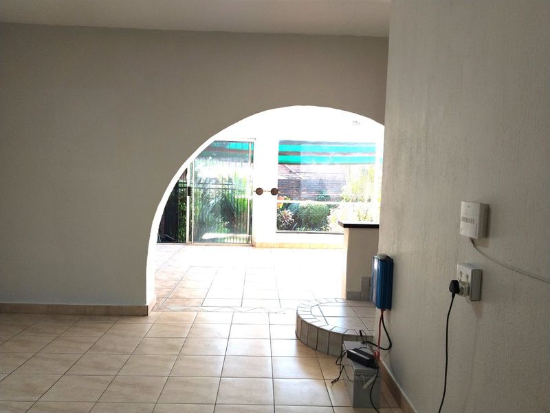 An empty living area featuring tiled flooring, an arched architectural opening, and direct access to an outdoor patio through a sliding glass door.