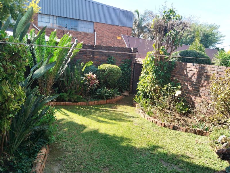 A private rear garden featuring a well-maintained lawn, established garden beds with brick edging, and secure brick boundary walls with electric fencing.