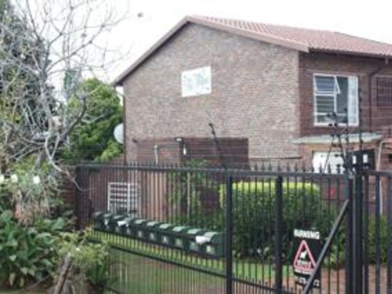 Front exterior view of a brick townhouse complex featuring a secure metal gate, electric fencing, and a row of communal post boxes.