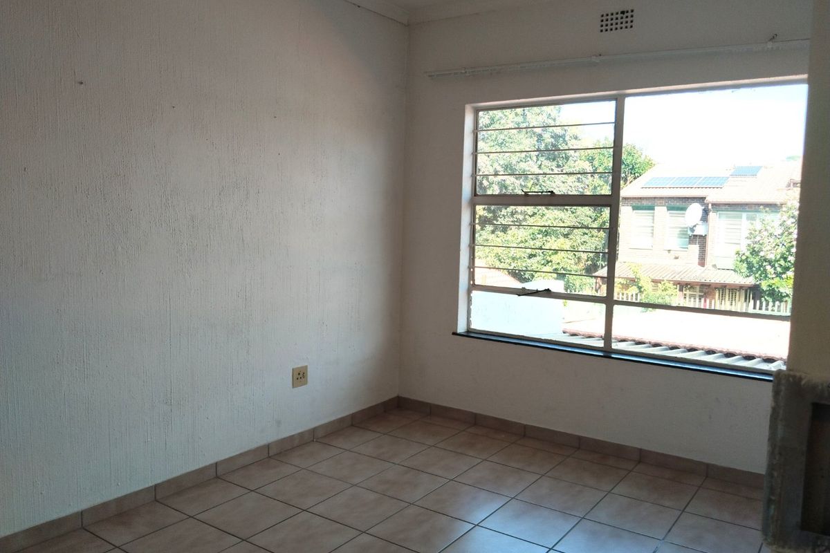 An empty bedroom featuring tiled flooring, a large window with security bars, and a ventilation grille, offering a blank canvas for potential updates.