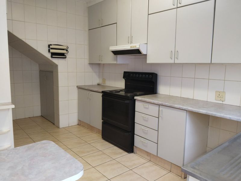 A functional kitchen featuring tiled flooring, ample built-in cabinetry, a freestanding electric stove with extractor fan, and convenient under-stair storage.
