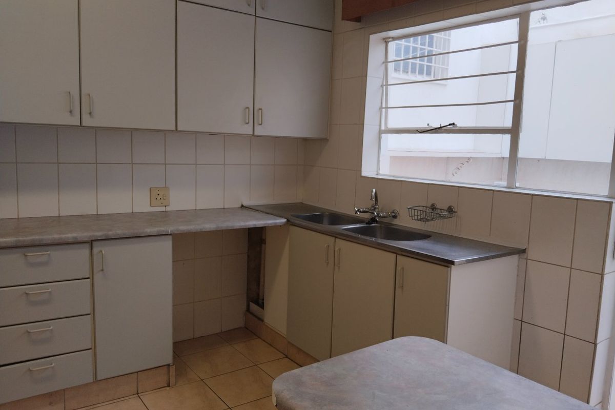 A functional kitchen featuring built-in cabinetry, laminate countertops, a double stainless steel sink, and tiled splashbacks, offering a blank canvas for modern updates.