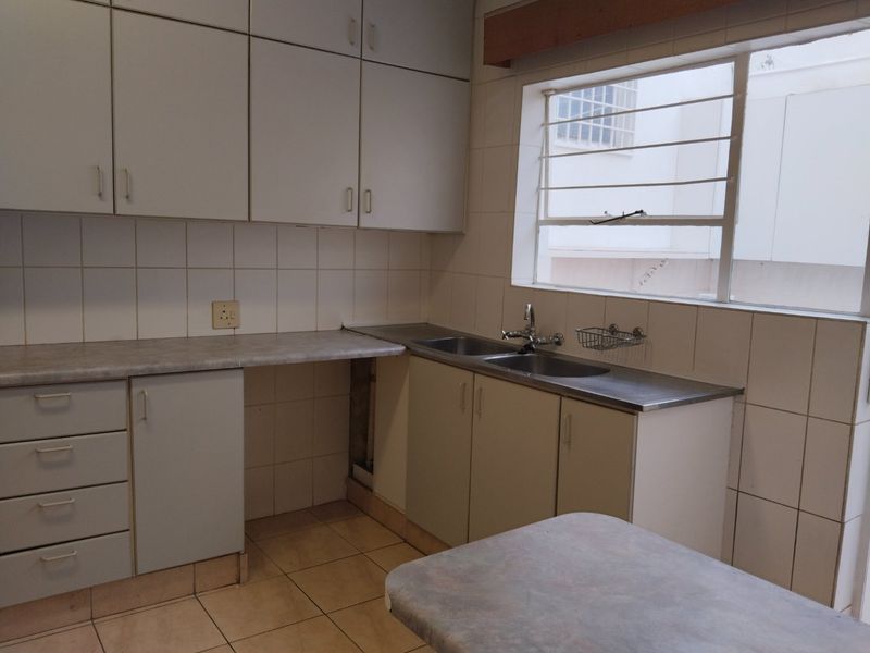 A functional kitchen featuring built-in cabinetry, laminate countertops, a double stainless steel sink, and tiled splashbacks, offering a blank canvas for modern updates.