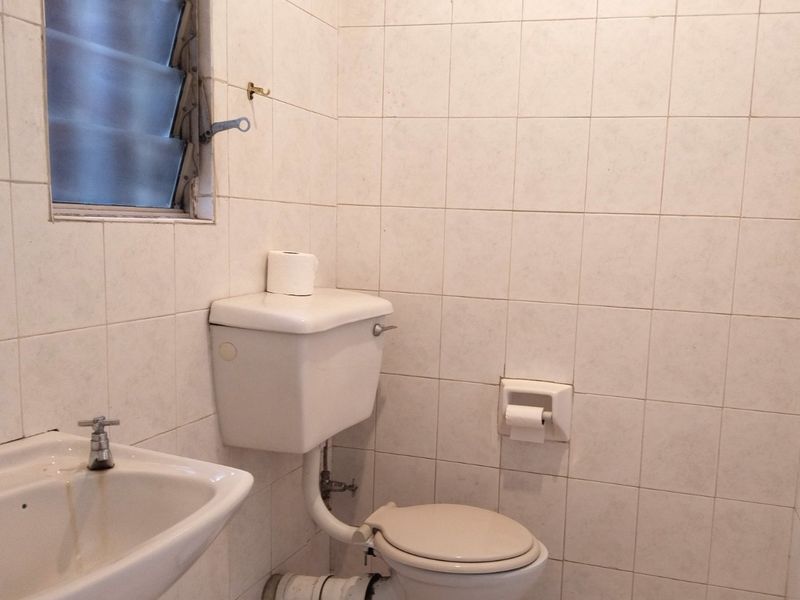 A dated bathroom featuring white ceramic wall tiles, a pedestal basin, and a standard close-coupled toilet with exposed plumbing.