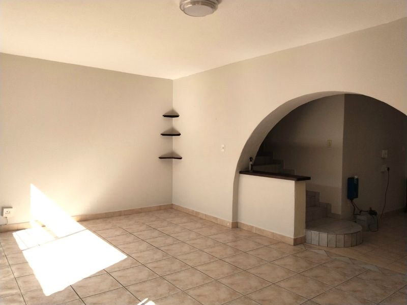 An empty living area featuring tiled flooring, an arched architectural detail leading to a staircase, and built-in corner shelving.