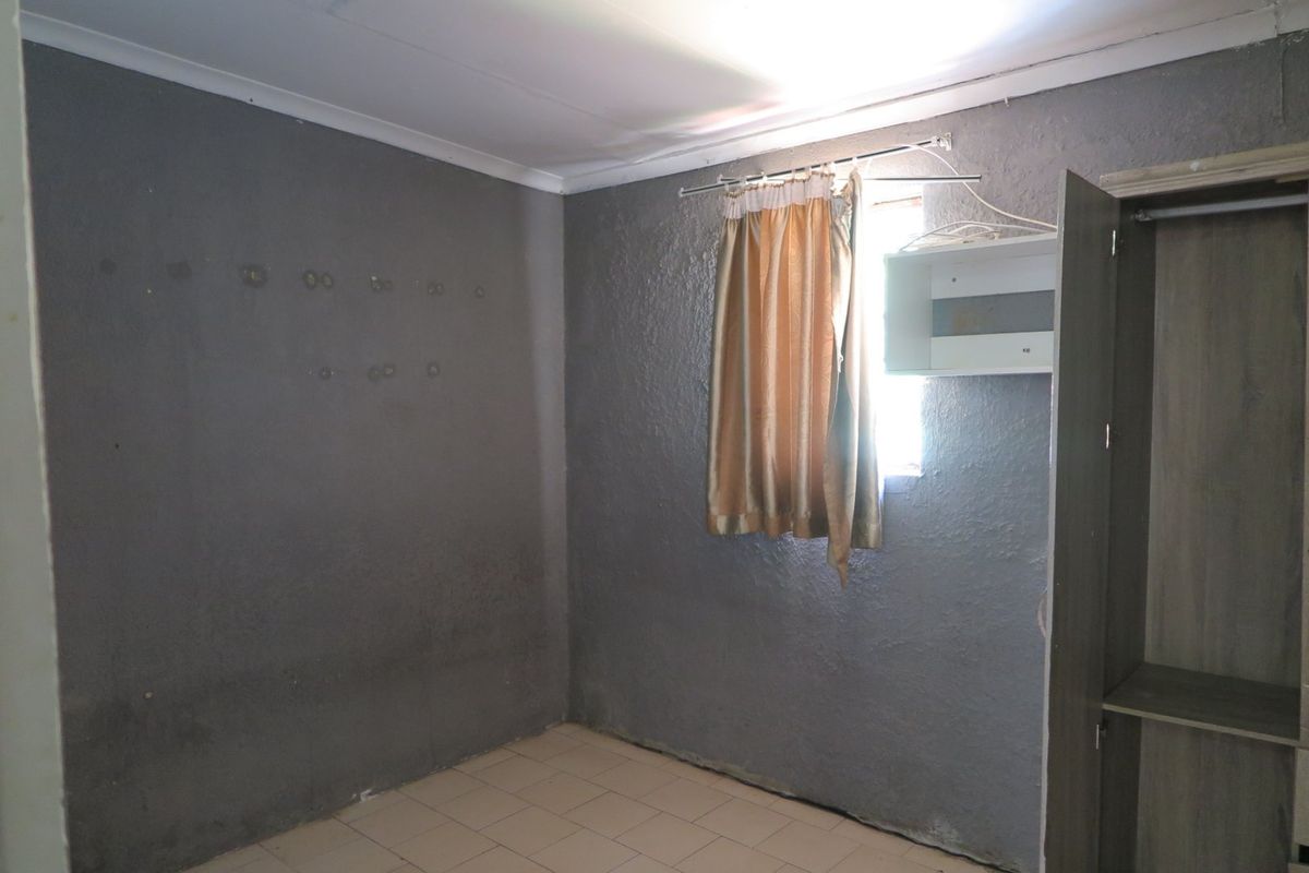 A vacant bedroom featuring tiled flooring, a built-in cupboard, and grey textured walls in need of cosmetic attention.