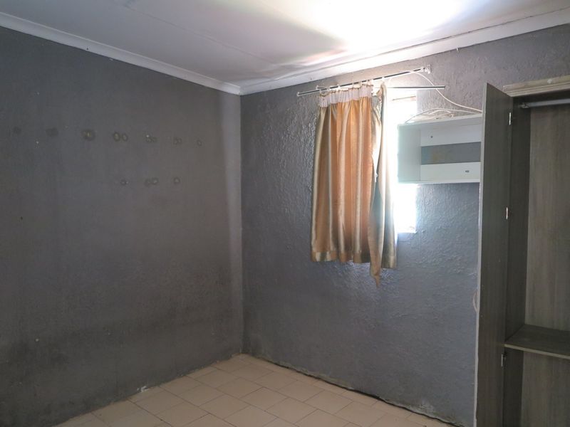 A vacant bedroom featuring tiled flooring, a built-in cupboard, and grey textured walls in need of cosmetic attention.