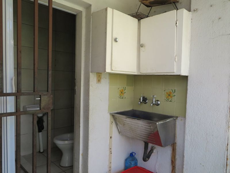 A functional laundry area featuring a stainless steel utility sink, wall-mounted cabinets, and an adjacent small bathroom with a toilet.