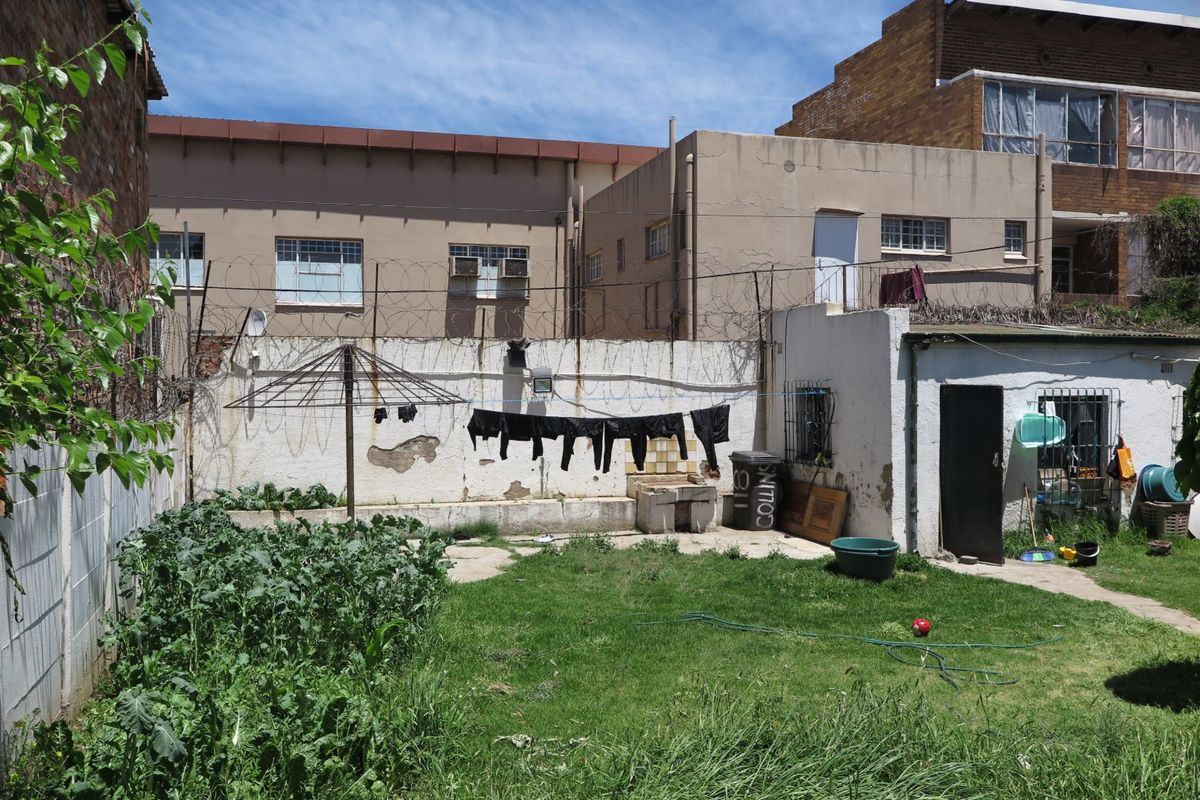 Rear garden area featuring a lawn, vegetable patch, and concrete boundary wall with security fencing.