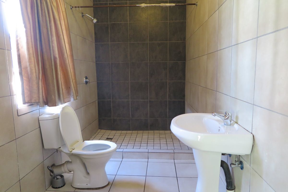 A functional bathroom featuring a walk-in shower, pedestal basin, and toilet with neutral wall and floor tiling.