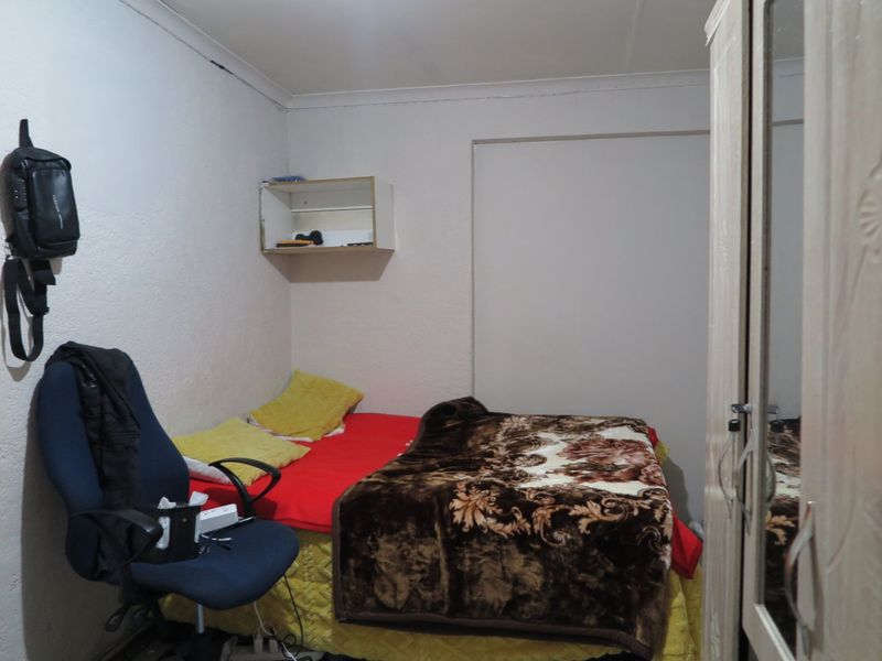 A compact bedroom featuring a built-in wardrobe and wall-mounted shelving, requiring minor cosmetic updates to the ceiling and wall finishes.