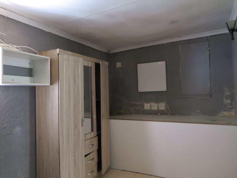 A bedroom space featuring grey walls with visible surface wear, a built-in cabinet, and wall-mounted electrical fixtures requiring cosmetic attention and finishing.