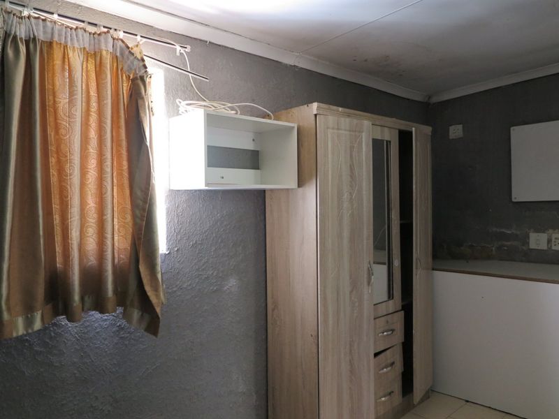 A bedroom space featuring textured grey walls, a window, and electrical points, requiring cosmetic updates and wall repairs to improve the overall condition.
