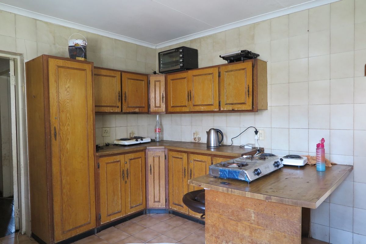A dated kitchen featuring wooden cabinetry, tiled backsplash, and tiled flooring, offering significant potential for modernization and renovation.