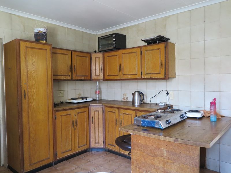 A dated kitchen featuring wooden cabinetry, tiled backsplash, and tiled flooring, offering significant potential for modernization and renovation.