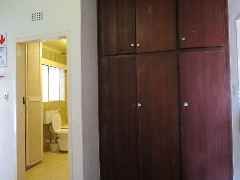 A bedroom featuring built-in wooden cupboards and an adjacent en-suite bathroom with dated fixtures.
