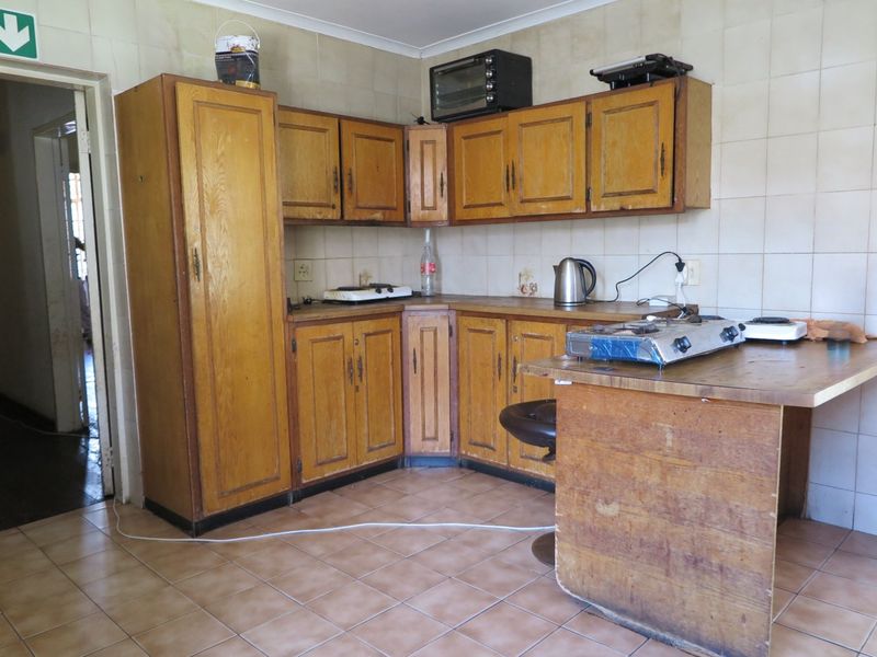 A dated kitchen featuring wooden cabinetry, tiled backsplash, and a built-in breakfast bar, offering significant potential for modernization and renovation.