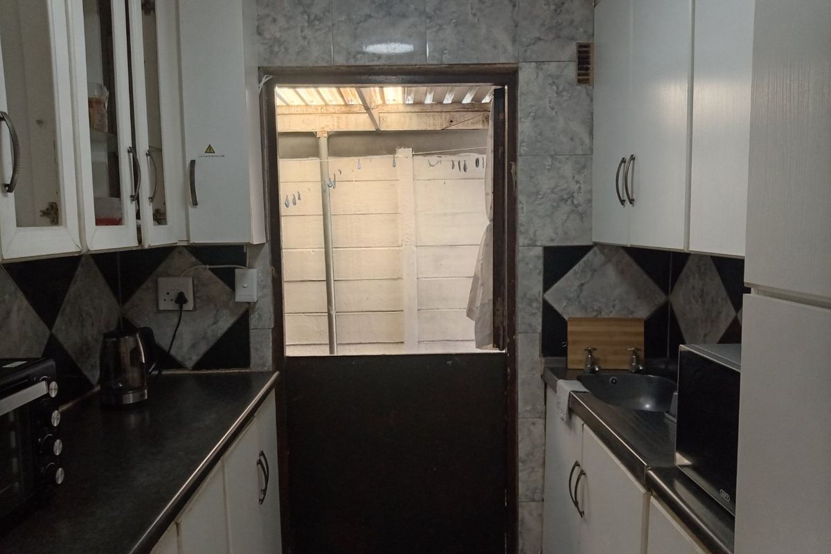 A compact kitchen featuring built-in cabinetry, laminate countertops, and a tiled backsplash, with a stable door leading to an outdoor area.