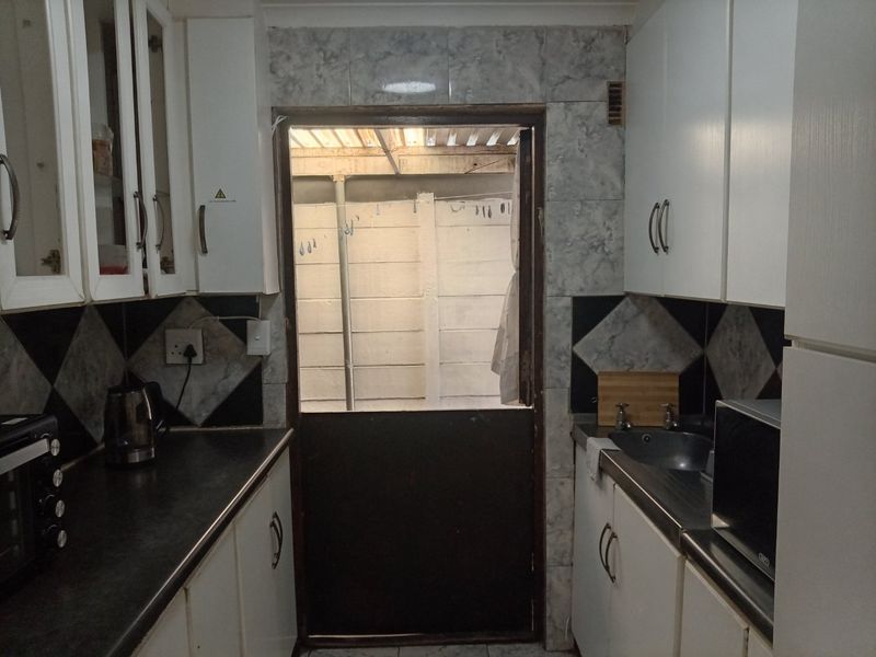 A compact kitchen featuring built-in cabinetry, laminate countertops, and a tiled backsplash, with a stable door leading to an outdoor area.
