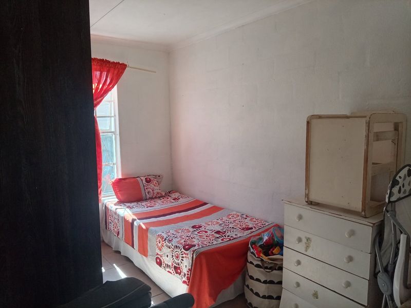 A compact bedroom featuring tiled flooring and a window with security bars, offering a functional space with potential for cosmetic updates.
