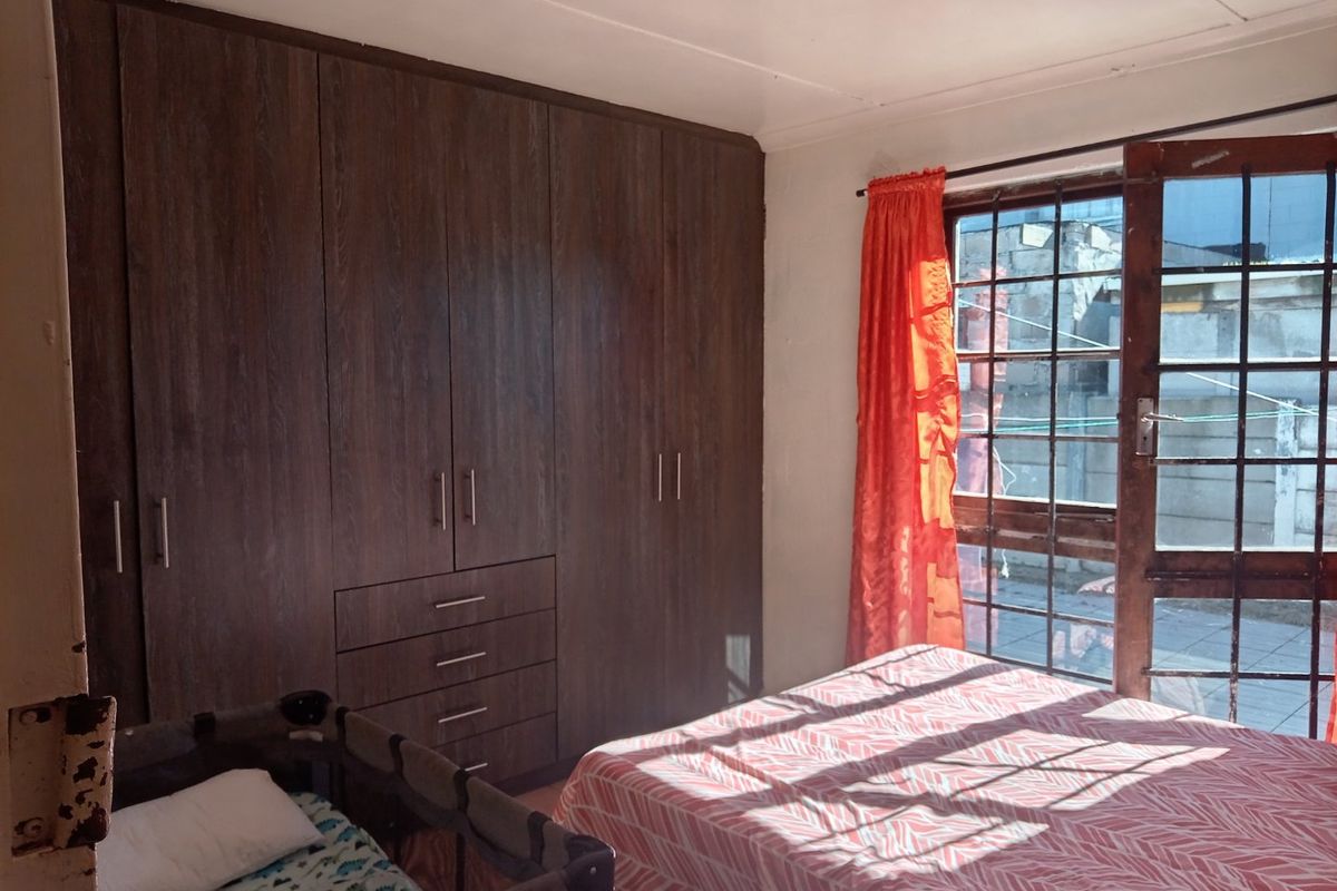 A bedroom featuring dark wood built-in cupboards and a window with security bars, providing natural light and storage space.