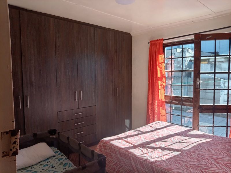 A bedroom featuring dark wood built-in cupboards and a window with security bars, providing natural light and storage space.