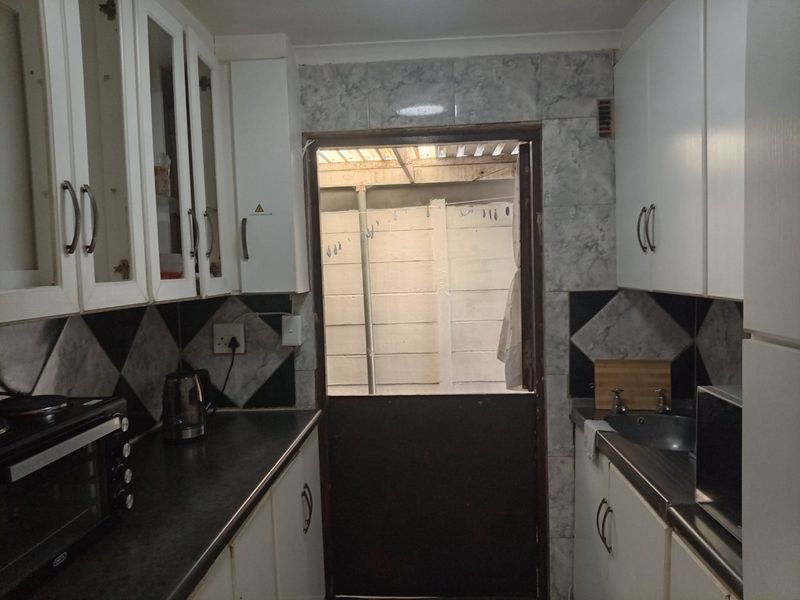 A compact galley-style kitchen featuring white cabinetry, dark countertops, and a stable door leading to an exterior utility area.