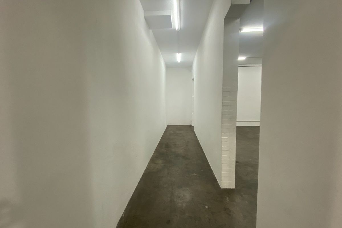 A functional industrial hallway or corridor space featuring painted walls, concrete flooring, and overhead fluorescent lighting fixtures.