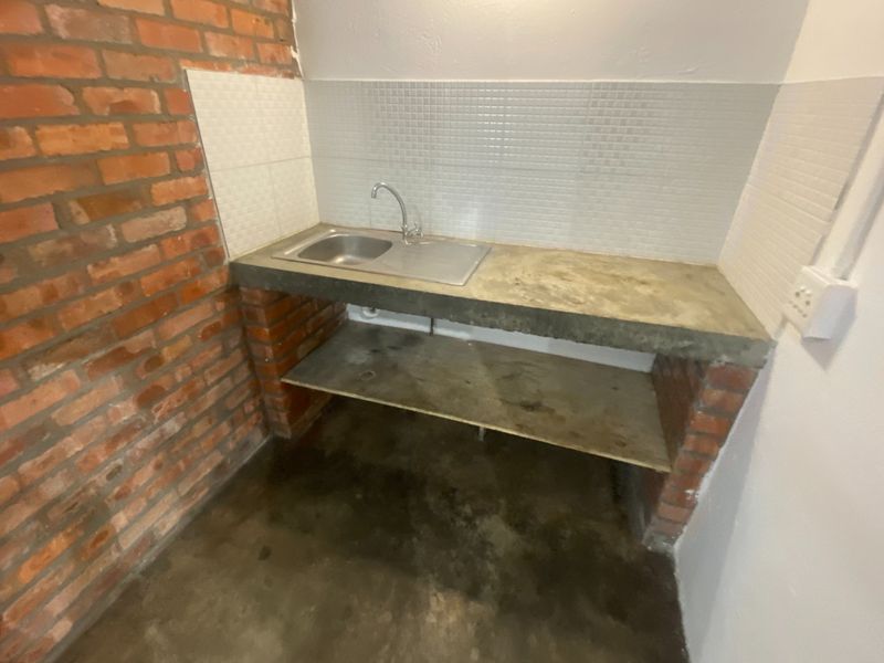 A basic utility or scullery area featuring a concrete countertop, stainless steel sink, and exposed brick wall finishes.