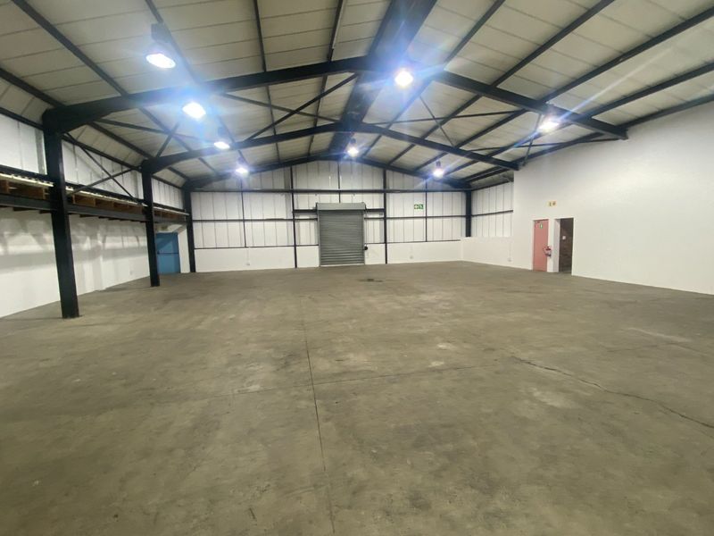 Spacious industrial warehouse unit featuring high ceilings, exposed steel trusses, concrete flooring, and a large roller shutter door for easy access.
