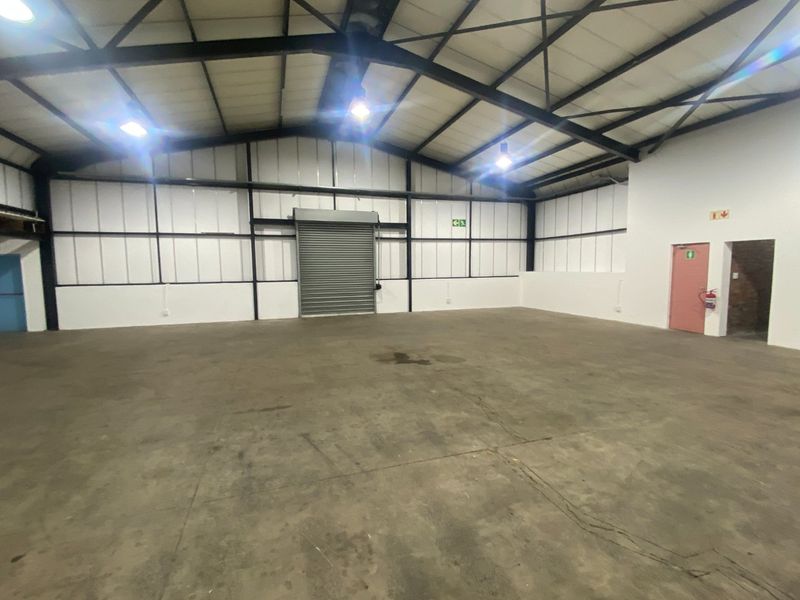Spacious industrial warehouse unit featuring high ceilings, exposed steel trusses, concrete flooring, and a large roller shutter door for easy access.