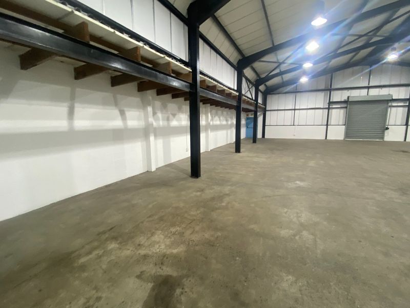 Spacious industrial warehouse unit featuring high ceilings, exposed steel structural beams, concrete flooring, and a large roller shutter door for easy access.